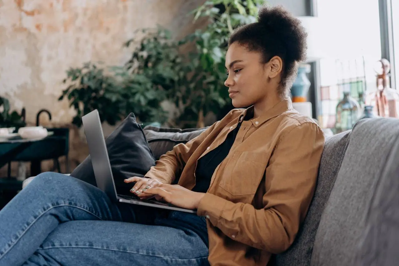 woman sitting on the sofa checking her uploads on the laptop in her lap